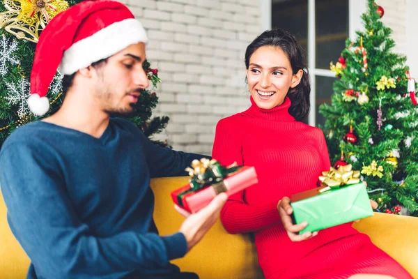 Noel Baba şapkalı romantik çift Noel ağacını süslerken ve yeni yılı kutlarken gülümserken ve birlikte vakit geçirirken eğleniyor. Adam kadınlara hediye kutusu sürprizi yapıyor.