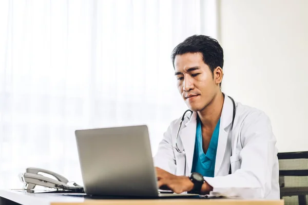 病院でノートパソコンを操作する聴診器と一様の制服を着たアジア人医師 — ストック写真