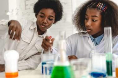 İki Afro-Amerikan tatlı oğlan ve kız öğrenci fen araştırması öğreniyor ve kimya bilimi deneyi yapıyor. Okulda test tüpünde sıvı karışımı yapıyorlar.