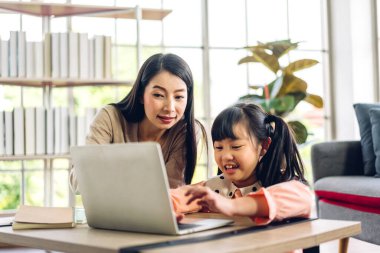 Anne ve Asyalı küçük kız öğreniyor ve online eğitim ile bilgisayar incelemesi yapıyor. Öğrenci evde eğitim bilgisini arıyor. Eğitim