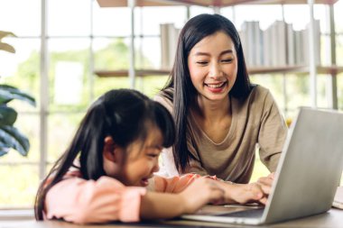 Anne ve Asyalı küçük kız öğreniyor ve online eğitim ile bilgisayar incelemesi yapıyor. Öğrenci evde eğitim bilgisini arıyor. Eğitim
