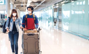 Coronavirus yüzünden karantinada olan genç mutlu bir çift cerrahi maske takıyor. Pasaport ve bilet, Uluslararası Terminal Havaalanı 'nda uzun süreli tatil uçuşundan önce.