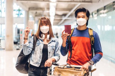 Coronavirus yüzünden karantinada olan genç mutlu bir çift cerrahi maske takıyor. Pasaport ve bilet, Uluslararası Terminal Havaalanı 'nda uzun süreli tatil uçuşundan önce.