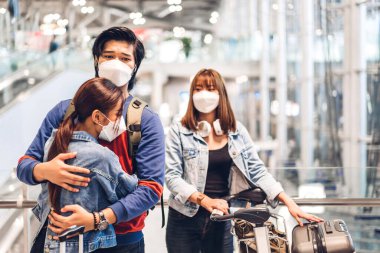 İki genç gezgin arkadaş, karantinada cerrahi maske takıp uluslararası havaalanında uzun bir tatil uçuşundan önce birbirlerine sarılıyorlar.