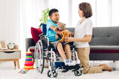 Asyalı fizyoterapistin portresi engelli çocuk sağlığı sorununa rehabilitasyon kliniğinde tekerlekli sandalyede oturarak yardım ve oyun oynayarak yardımcı oluyor.