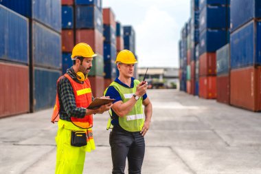 Kasklı profesyonel mühendis kargo ekibi ayakta çalışıyor ve telsiz kullanıyor. Stokları yükleme için konteynıra koyuyorlar. Lojistik ulaşım ve iş sektörü ihracatı.