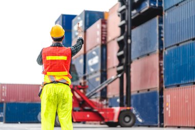 Kasklı profesyonel mühendis konteynır ustabaşı ayakta çalışıyor ve telsiz kullanıyor. Stokları yükleme için konteynıra koyuyor. Lojistik ulaşım ve iş sektörü ihracatı