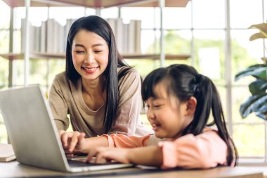 Anne ve Asyalı küçük kız öğreniyor ve online eğitim ile bilgisayar incelemesi yapıyor. Öğrenci evde eğitim bilgisini arıyor. Eğitim
