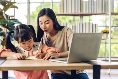 Anne ve Asyalı küçük kız öğreniyor ve online eğitim ile bilgisayar incelemesi yapıyor. Öğrenci evde eğitim bilgisini arıyor. Eğitim