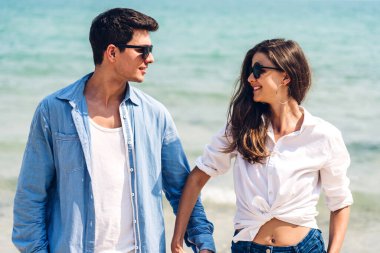 Romantik aşk genç mutlu gülümseme balayı seyahati çift mavi gökyüzü deniz plajında kum üzerinde duruyor birlikte eğleniyorlar ve tropikal plajda dinleniyorlar.
