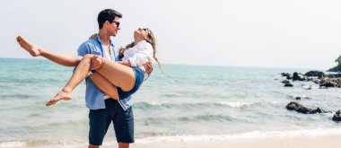 Romantik aşk genç mutlu gülümseme balayı seyahati çift mavi gökyüzü deniz plajında kum üzerinde duruyor birlikte eğleniyorlar ve tropikal plajda dinleniyorlar.