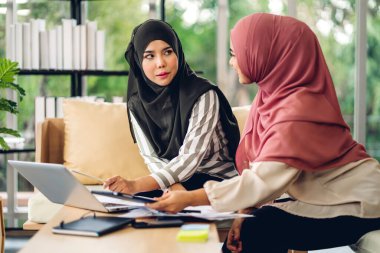 Gülümseyen mutlu Asyalı güzel Müslüman kadın dizüstü bilgisayarla rahatlıyor, çalışıyor ve analiz ediyor. Başlangıç projesi planı ve evdeki beyin fırtınası ile strateji tartışıyorlar.