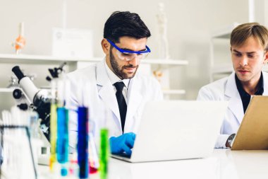 Profesyonel iki bilim adamı test tüpünde sıvı analiz ederken ve karıştırırken kimyasal bir deney yapıyor. Genç bilim adamı laboratuvarda cam üzerine kimyasal örnekler bırakıyor.