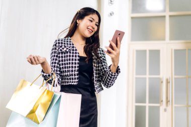 Gülümseyen güzel Asyalı moda mutlu kadın portresi rahatla ve alışveriş zamanının tadını çıkar yaz yürüyüşü ve alışveriş renkli bir çanta al bir şeyler almak için mağazada akıllı telefon kullan