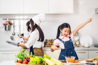 Mutlu bir aşk portresi. Asyalı bir anne ve küçük Asyalı bir kız çocuk. Mutfakta taze sebze salatası ve sandviç malzemesiyle birlikte sağlıklı yemekler pişirmeye yardım ediyorlar.