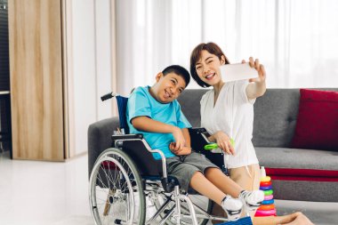 Mutlu aşk portresi. Asyalı anne oynuyor ve bakıcı tekerlekli sandalyede oturan engelli çocuğa bakıyor. Evde engelli bakımı konseptinde iyi vakit geçiriyor.