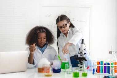 Bir grup genç öğrenci kimyasal bir deney yapıyor ve deney tüpünü el ele tutuyorlar. Laboratuvar sınıfında, okuldaki masada. Eğitim konsepti.