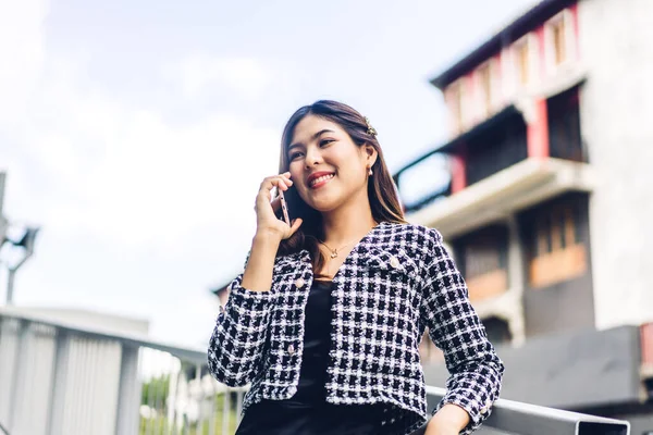 Gülümseyen mutlu Asyalı iş kadınının portresi dijital teknoloji akıllı telefon kullanarak rahatlıyor. Genç Asyalı kız iş yeri arıyor ve şehirdeki iş arkadaşlarıyla konuşuyor.