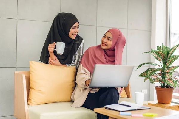 Gülümseyen mutlu Asyalı güzel Müslüman kadın dizüstü bilgisayarla rahatlıyor, çalışıyor ve analiz ediyor. Başlangıç projesi planı ve evdeki beyin fırtınası ile strateji tartışıyorlar.