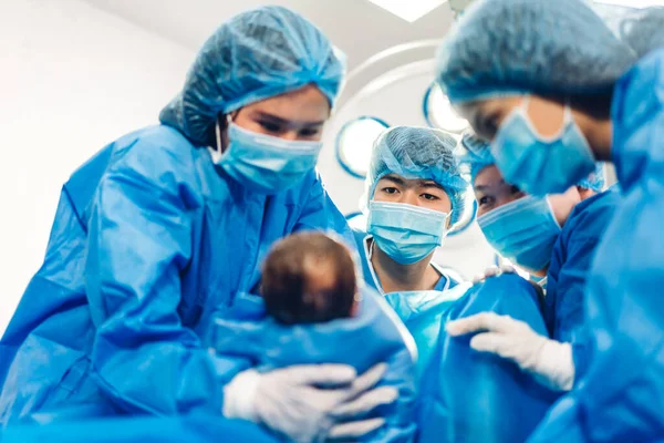 Profesyonel anestezi uzmanı doktor tıbbi ekip ve asistan bebek sezaryeni yapıyor ve bebeği modern hastane ameliyathanesinde doğum ekipmanıyla doğuruyor.
