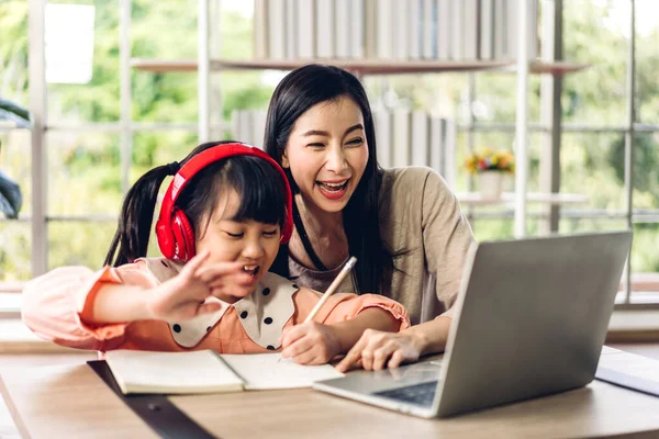 Anne ve Asyalı küçük kız öğreniyor ve online eğitim ile bilgisayar incelemesi yapıyor. Öğrenci evde eğitim bilgisini arıyor. Eğitim