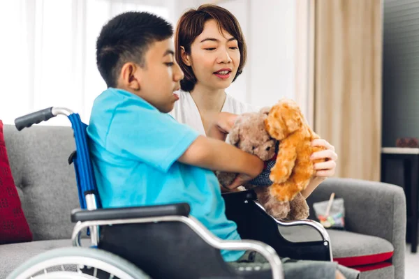 Portrait of enjoy happy love family asian mother playing and carer helping look at disabled son child sitting in wheelchair moments good time at home.disability care concept