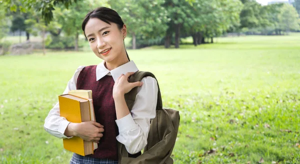 Smiling woman international student or teenager standing and holding book look at camera in park at university.Education Concept