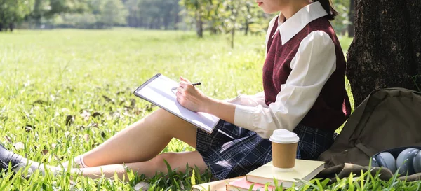 美学生や十代のアジアの女性の肖像は 大学で公園に座っている間 紙の本の仕事の研究とページ雑誌を見て学ぶ読みます — ストック写真