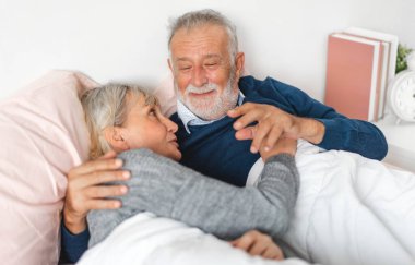 Senior happy love elder couple relaxing and talking together lying on bed in bedroom at home.Retirement healthcare couple concept