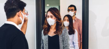 Bir grup profesyonel Asya işi ve ofiste koruyucu maske takarak koronavirüs için karantinada çalışmadan önce vücut ısısını ölçmek için kızılötesi termometre kullanılıyor.