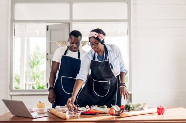Afro-Amerikan bir çiftin portresi. Evde mutfakta lezzetli yemekler hazırlamak için taze sebze salatası ve sandviç malzemeleriyle birlikte yemek pişiriyorlar.