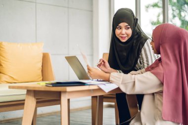 Gülümseyen mutlu Asyalı güzel Müslüman kadın dizüstü bilgisayarla rahatlıyor, çalışıyor ve analiz ediyor. Başlangıç projesi planı ve evdeki beyin fırtınası ile strateji tartışıyorlar.