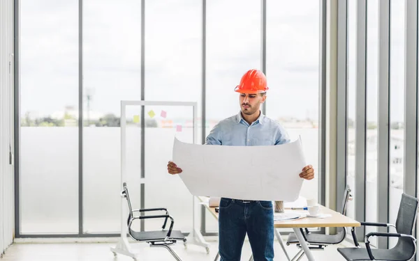 Professional of architect industrial engineer cargo man in helmet working new construction project architectural plan with blueprint and construction tool on table at the building construction site