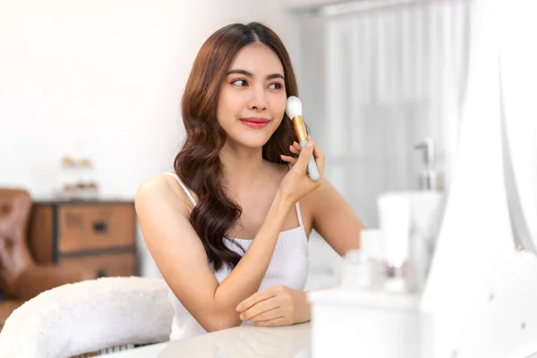 Smiling of young beautiful pretty asian woman clean fresh healthy white skin looking at mirror.asian girl holding make-up brushes and make up on face with cosmetics set at home.facial beauty