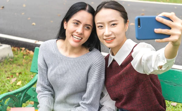 Smiling group of friend woman international student or teenager standing and look at camera making live selfie on smartphone in travel vacation summer park.selfie time and friendship Concept