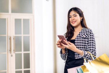 Gülümseyen güzel Asyalı moda mutlu kadın portresi rahatla ve alışveriş zamanının tadını çıkar yaz yürüyüşü ve alışveriş renkli bir çanta al bir şeyler almak için mağazada akıllı telefon kullan