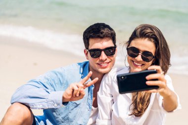 Romantik aşk genç mutlu gülümseme balayı çifti mavi gökyüzü kumsalındaki kumsalda tatil gezisinde tropikal sahilde birlikte eğleniyor ve dinleniyorlar.