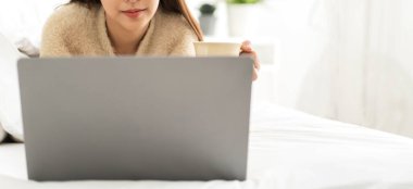 Genç gülümseyen mutlu Asyalı kadın evdeki yatak odasında dizüstü bilgisayar kullanarak rahatlıyor. Ev konseptinden çalışıp klavyede yazan genç yaratıcı kız.