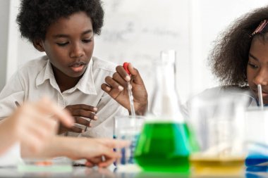 İki Afro-Amerikan tatlı oğlan ve kız öğrenci fen araştırması öğreniyor ve kimya bilimi deneyi yapıyor. Okulda test tüpünde sıvı karışımı yapıyorlar.