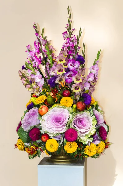 An unexpected original bouquet of flowers, vegetables and fruits mounted on a pedestal in a copper vase.