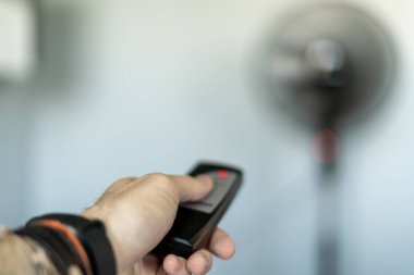 Sıcak hava dalgasının ortasında uzaktan kumandayla vantilatörü açan biri.