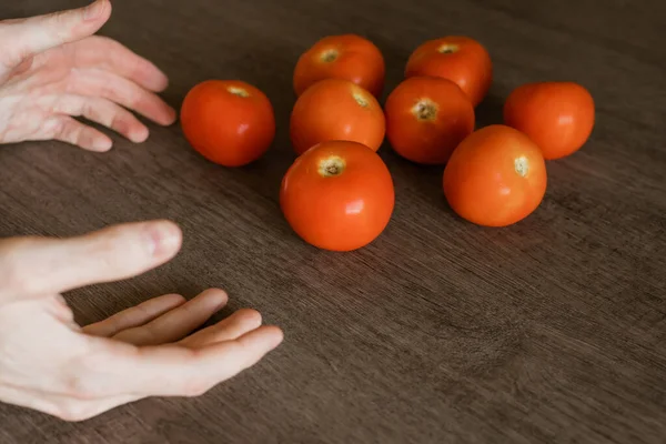 Man\'s hands about to pick a few organic tomatoes that are perched on the wooden table in his kitchen.