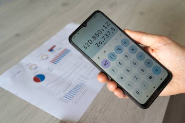 Man's hand holding a calculator to analyze and check the results and rates of the company