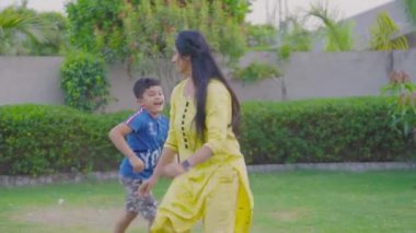 Indian Mother with her cute son, child playing together, running, chasing, hugging, laughing, having fun, joy making face expressions in beautiful green garden. Mother's Day concept.Slow motion