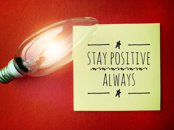 Image with motivational quotes on sticky note with bright shinning bulb and red color background - Stay positive always. — Fotografia de Stock