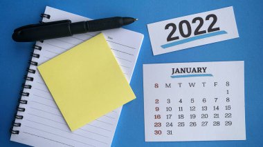 Beyaz Ocak 2022 takvimi, yapışkan not, siyah kalem ve not defteri arkaplanı. 2022 Yeni Yıl Konsepti