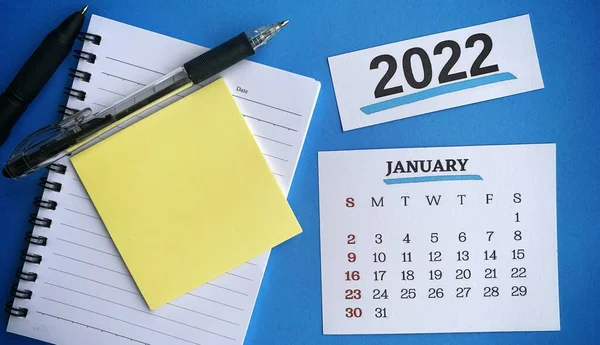Biały kalendarz styczniowy 2022 z lepką nutą, długopisem i notatnikiem. Koncepcja nowego roku 2022 — Zdjęcie stockowe
