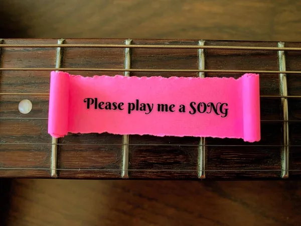 Please play me a song text written on a small piece of torn paper with guitar background. Music concept. — Stockfoto