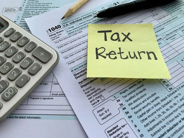 Close up on hand written tax return on sticky note with 1040 tax form, pen, pencil and calculator. Taxation concept.