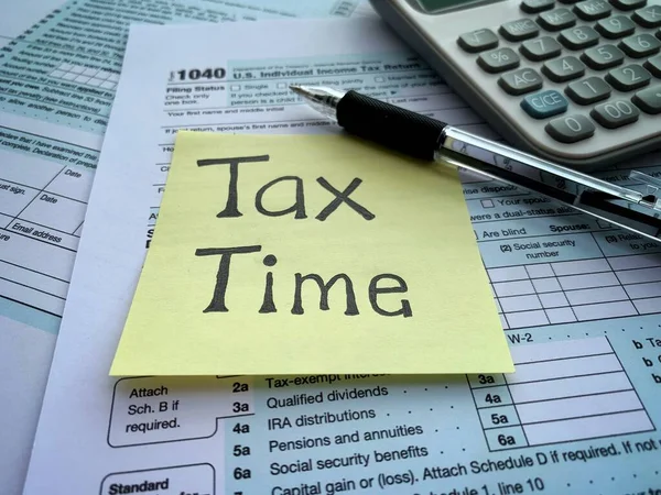 Close up on tax time text on sticky note with 1040 tax form, pen and calculator. Conceptual. — Foto Stock